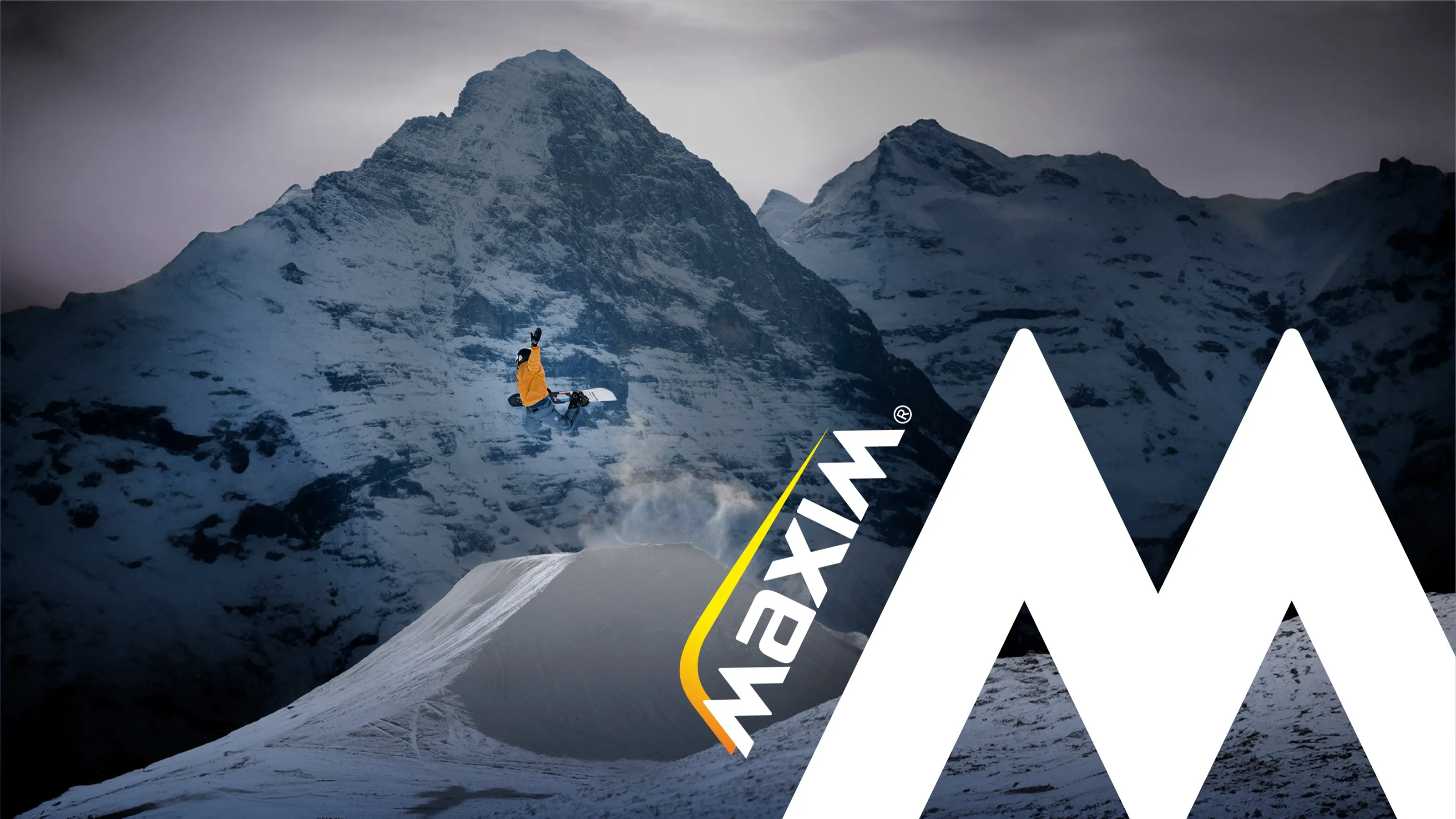 Snowboarder mid-jump in front of snowy mountains, with the Maxim logo and large white M