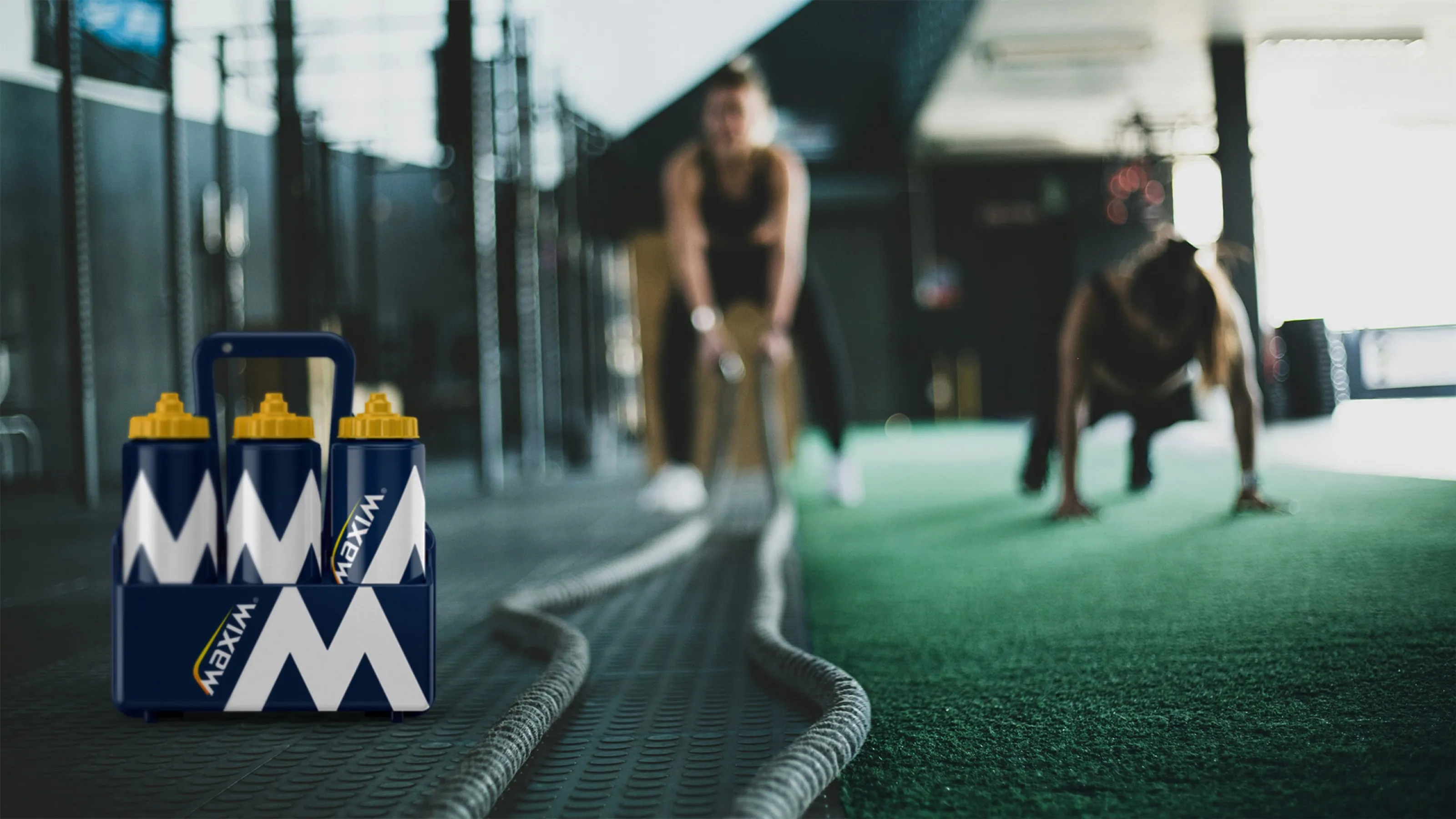 Maxim water bottles in a carrier on a gym floor, with people training in the background