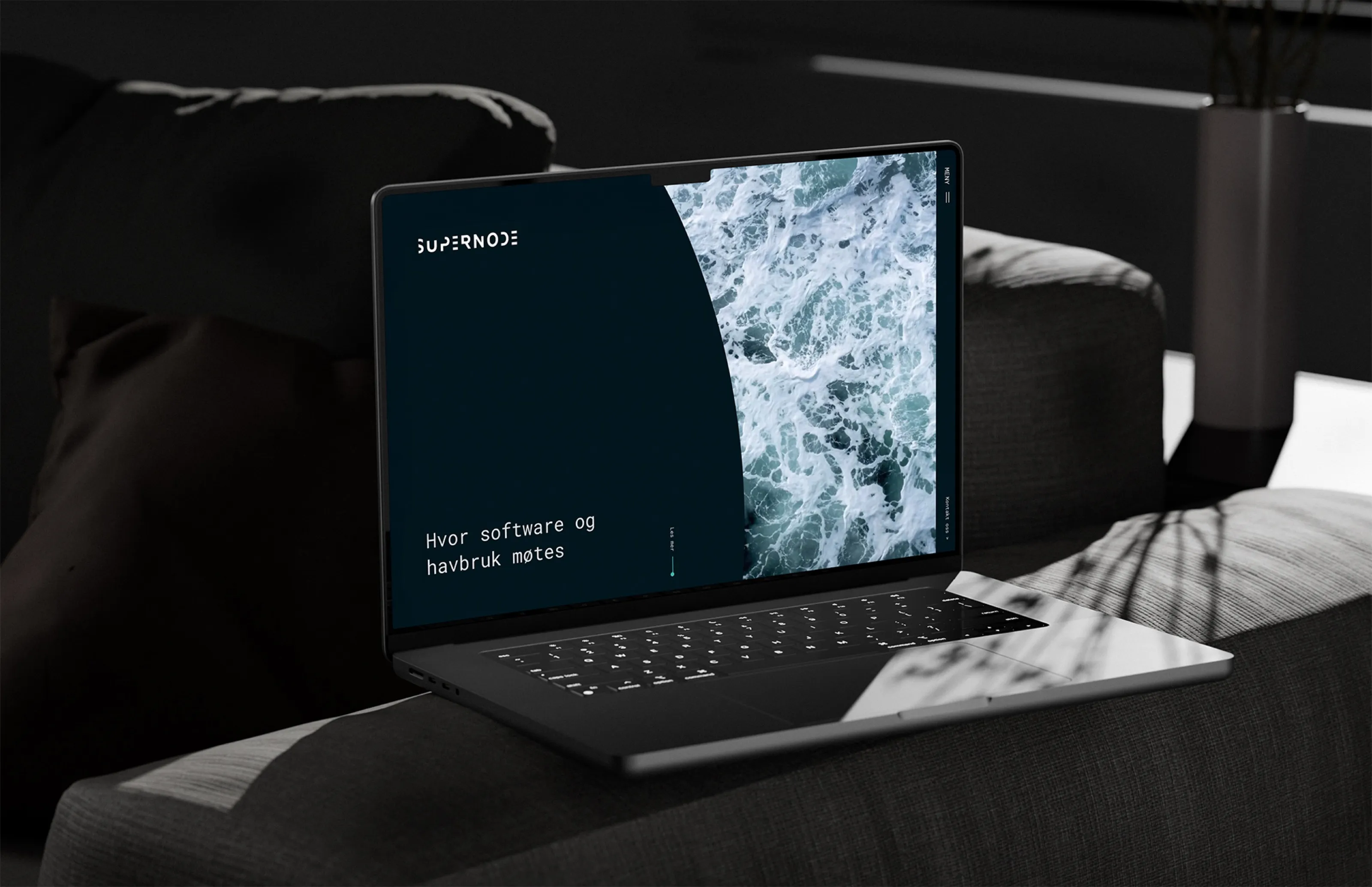 Laptop on a sofa showing the Supernode homepage: “Hvor software og havbruk møtes” beside ocean foam