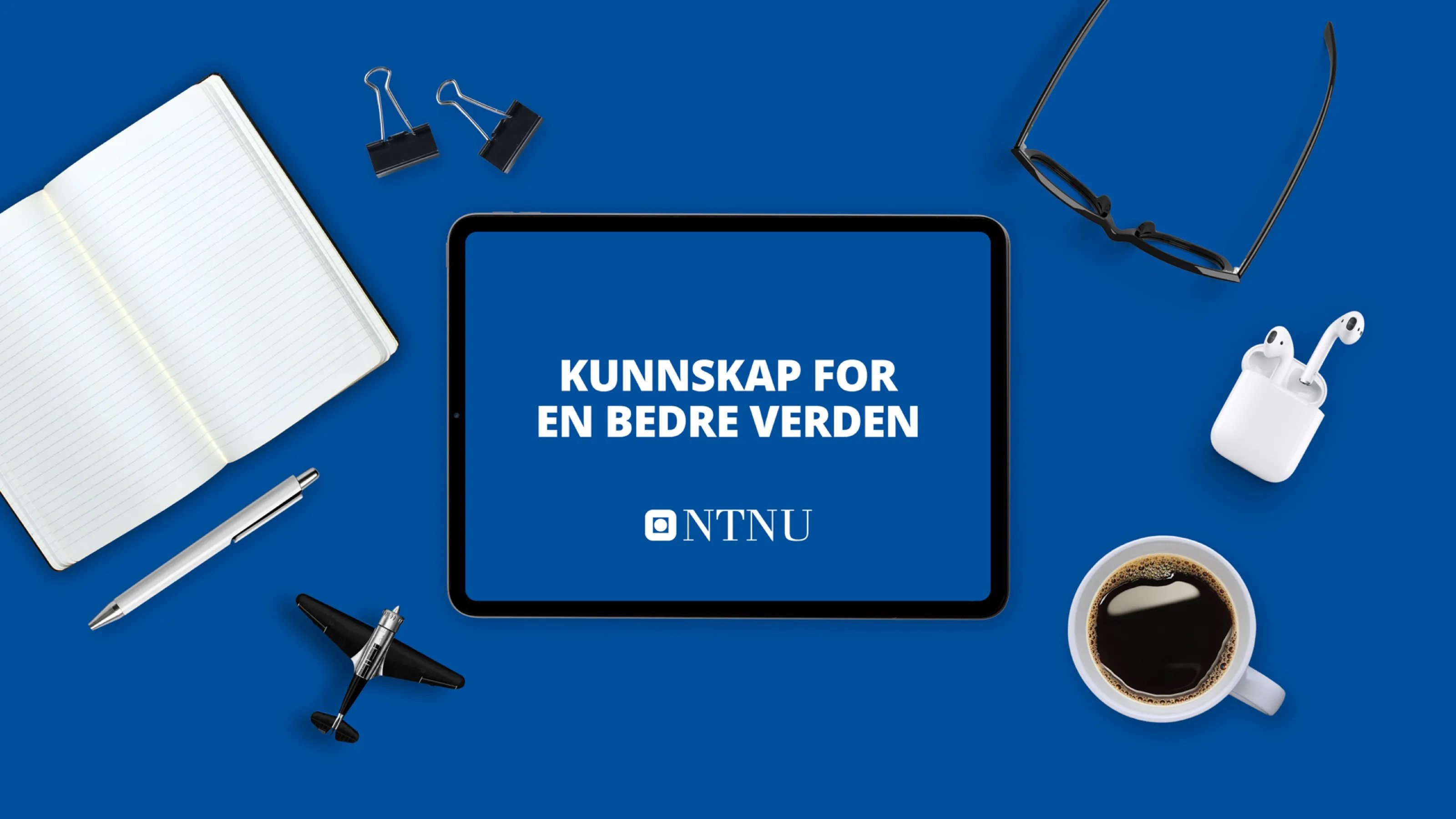 Tablet showing NTNU’s slogan “Kunnskap for en bedre verden” on a blue desk with notebook and coffee