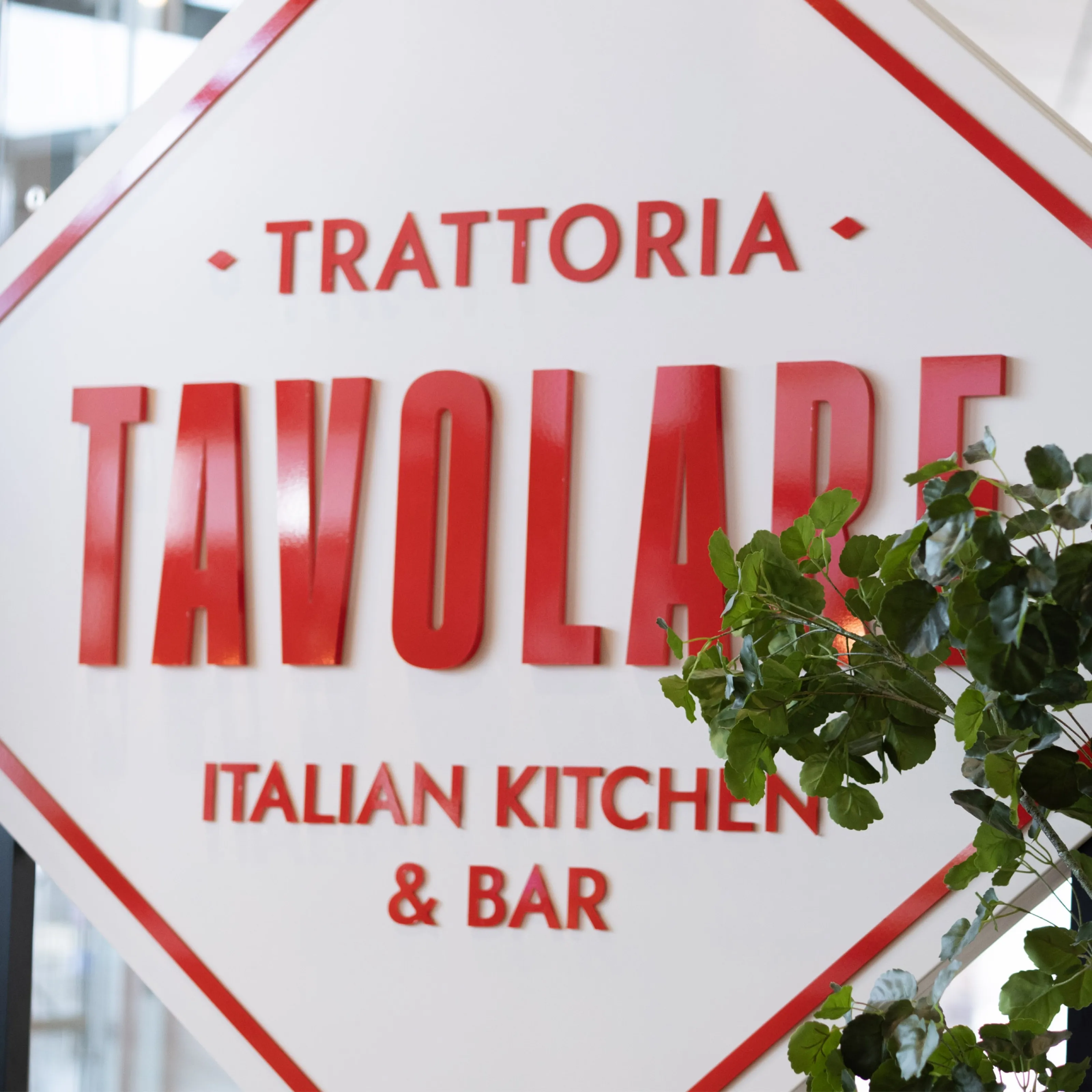 Close-up of the red Trattoria Tavolare “Italian kitchen & bar” sign with green leaves