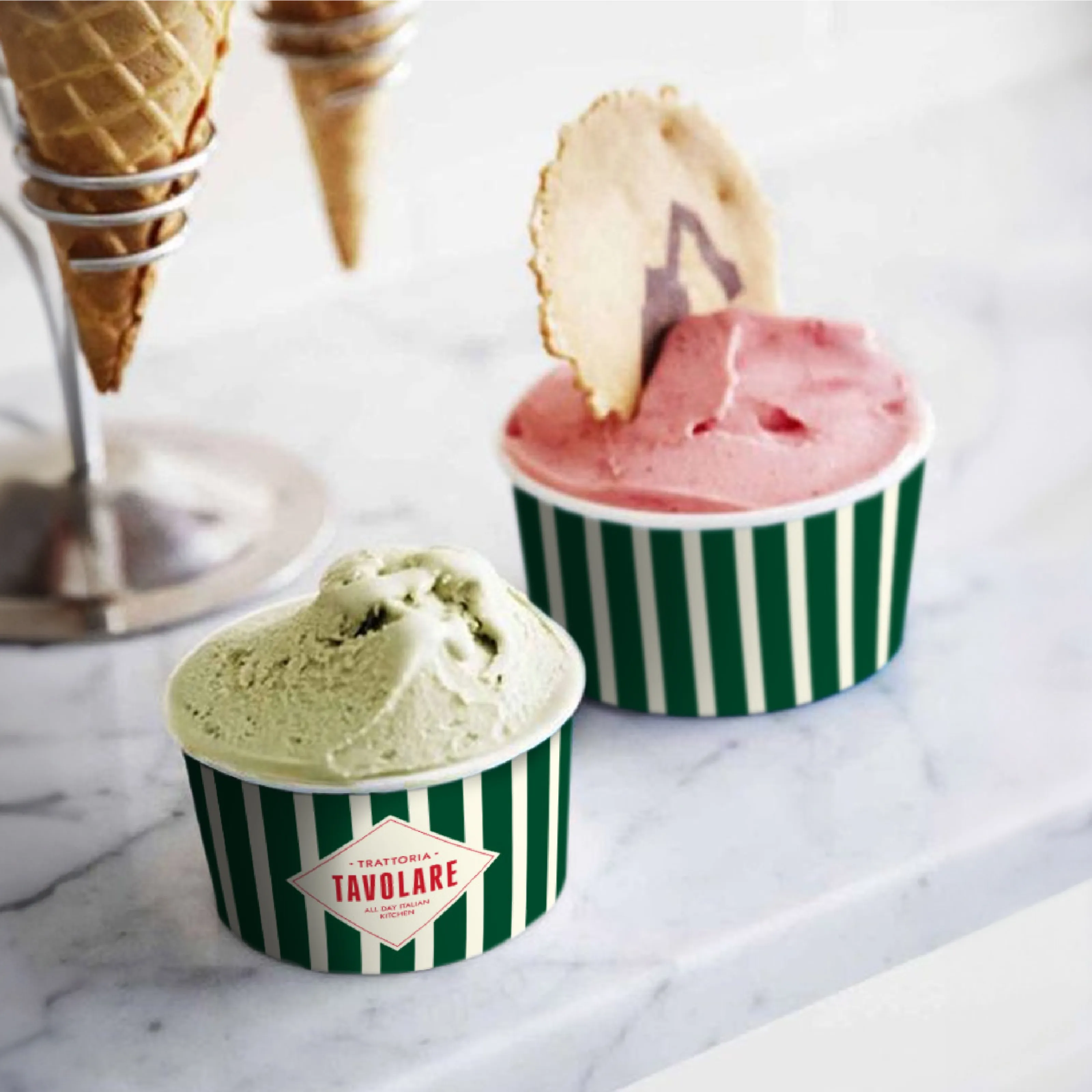 Pistachio and strawberry gelato in green-and-white striped Tavolare cups on marble