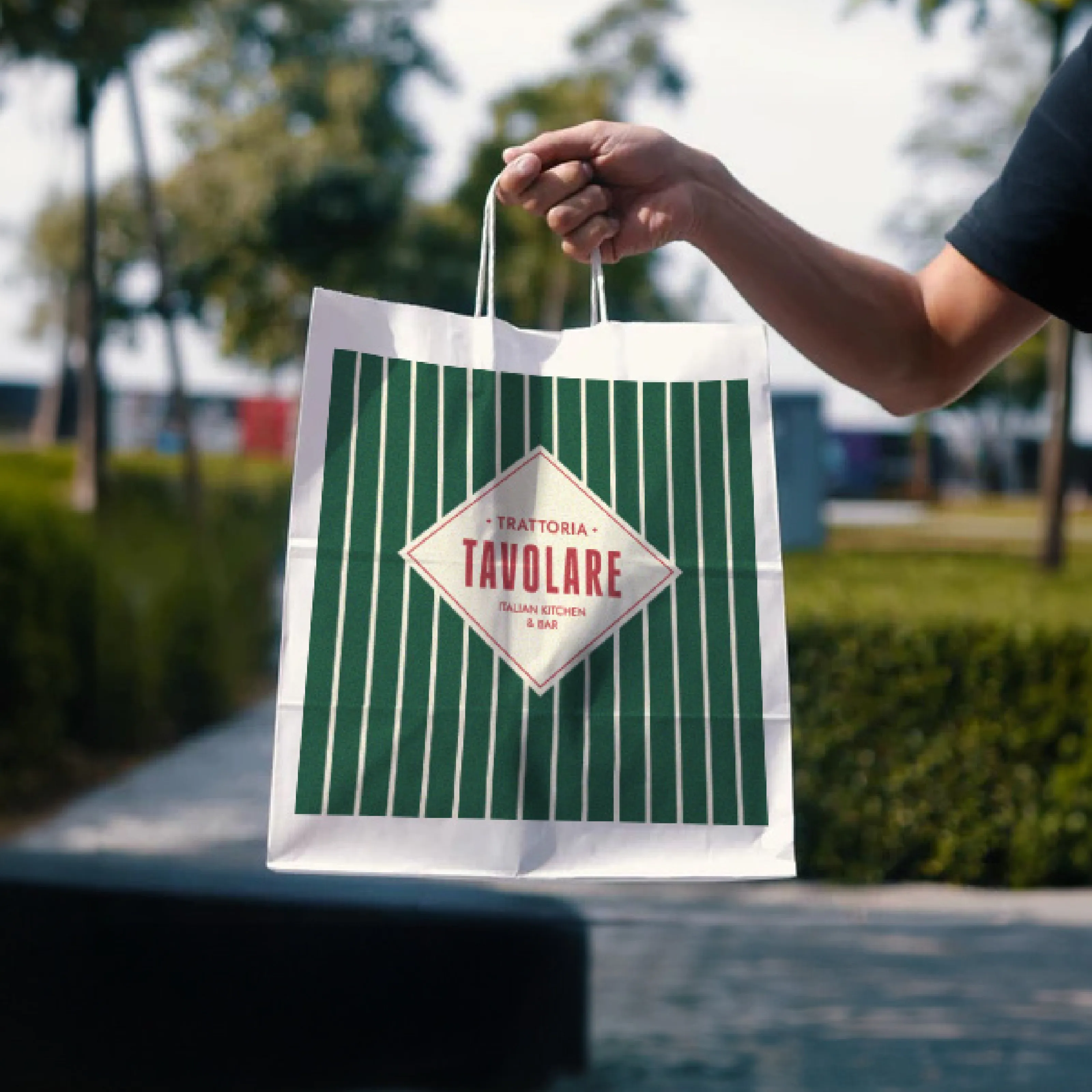 Hand holding a green-and-white striped Tavolare paper bag with the diamond logo